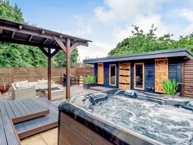 An outdoor patio with a hot tub wooden pergola seating area and a dark wooden cabin at Orchard Retreat Staycation in Kirton