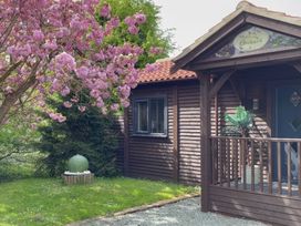 A wooden cabin with a porch and a potted plant next to a flowering tree at Orchard Retreat Staycation in Kirton