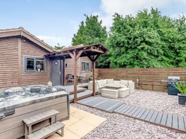 An outdoor patio area with a hot tub wooden deck table with chairs cushioned seating area barbecue grill and wooden fence surrounded by trees at Orchard Retreat Staycation in Kirton