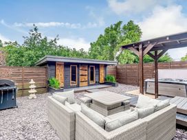 An outdoor patio with a wicker sofa set around a table a barbecue grill and a wooden structure covering a hot tub at Orchard Retreat Staycation in Kirton
