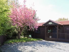 A wooden building with a covered porch and a pink flowering tree beside it at Orchard Retreat Staycation in Kirton