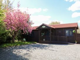 A small wooden cabin with a red tiled roof next to a pink blossoming tree at Orchard Retreat Staycation Kirton
