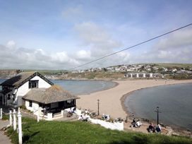 A beach scene with a house near the water and people sitting at the shoreline at Apartment 12, Burgh Island Causeway Bigbury-On-Sea