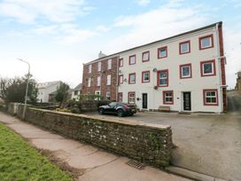 An exterior view of a two-story building with red trimmed windows and black doors with a car parked outside at Flat 6 Aikbank in Whitehaven