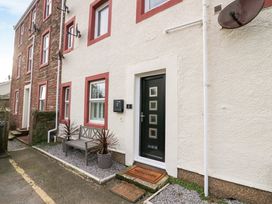 The exterior entrance of a property with a black door, a welcome mat, a bench with two potted plants and windows with red frames at Flat 6 Aikbank in Whitehaven