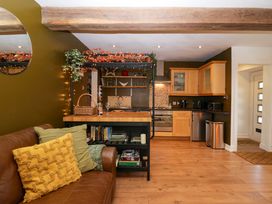 A kitchen and living area with wooden cabinets a brown leather sofa with cushions and wooden beams at Flat 6 Aikbank in Whitehaven