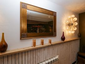 A wooden shelf with glass candle holders and decorative vases under a framed mirror and wall light at Flat 6 Aikbank in Whitehaven