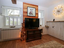 A room with a television on a wooden cabinet two windows with shutters and a dog picture on a wooden panel wall at Flat 6 Aikbank in Whitehaven