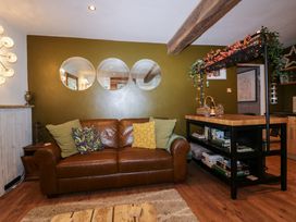 A living room with a brown leather sofa and pillows next to a kitchen island with books and bottles at Flat 6 Aikbank in Whitehaven