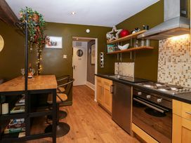 A kitchen with wooden shelves and cabinets a dining table with two chairs and a cooking area with stove and oven at Flat 6 Aikbank in Whitehaven