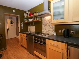 A kitchen with wooden cabinets black countertop electric stove and oven a black kettle and open shelving at Flat 6 Aikbank in Whitehaven