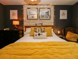 A bedroom with a bed with yellow bedding and cushions a black dresser with a lamp and framed pictures on the wall at Flat 6 Aikbank in Whitehaven