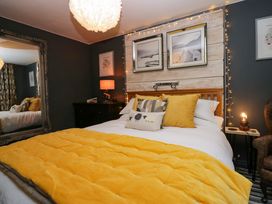 A bedroom with a bed covered in yellow bedding and cushions with framed pictures and fairy lights on the wall at Flat 6 Aikbank in Whitehaven