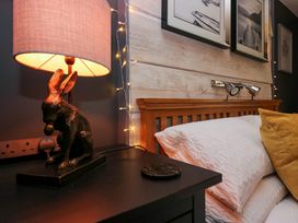 A bedside table with a lamp featuring a rabbit base next to a bed with white pillows and a yellow cushion at Flat 6 Aikbank in Whitehaven