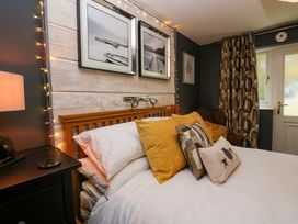 A bedroom with a wooden bed frame white bedding yellow and patterned pillows black nightstand with lamp and framed pictures on the wall at Flat 6 Aikbank in Whitehaven
