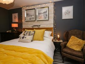 A bedroom with a bed with yellow pillows and blanket an armchair with a yellow cushion a bedside table with a lamp and framed pictures on the walls at Flat 6 Aikbank in Whitehaven