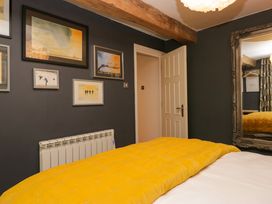 A bedroom with a yellow bedspread a wall with framed pictures a radiator a large mirror and a wooden beam at Flat 6 Aikbank in Whitehaven
