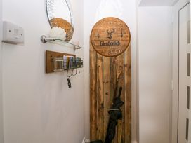 A hallway with a round mirror and shelf above a key holder and a wooden coat rack with hooks and an umbrella at Flat 6 Aikbank in Whitehaven