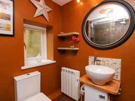 A bathroom with a toilet a round mirror shelves with flowers and a vessel sink at Flat 6 Aikbank in Whitehaven