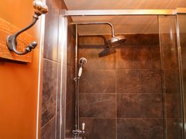 A shower area with large brown tiles a rain showerhead a handheld shower and a wall hook with a decorative knob at Flat 6 Aikbank in Whitehaven