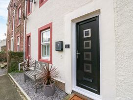 The exterior of a house with a black door featuring square windows a bench between two potted plants and red trimmed white walls at Flat 6 Aikbank in Whitehaven