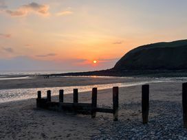 A beach scene with wooden posts on the sand and a hill in the background at sunset at Flat 6 Aikbank in Whitehaven