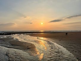 A beach with a small stream of water flowing toward the sea at sunset with a dog standing on the sand at Flat 6 Aikbank in Whitehaven