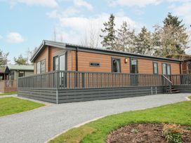 An exterior view of a brown wooden cabin with a gray deck and railing surrounded by grass and trees at Peony in Eardisland