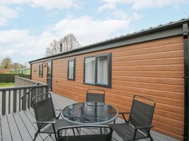 An outdoor deck with a round glass table and four black chairs beside a brown building at Peony in Eardisland