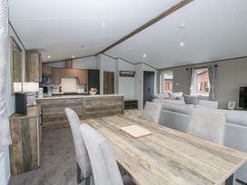 An open living area with a wooden dining table, upholstered chairs, a sofa, kitchen cabinets, and windows with curtains at Peony in Eardisland