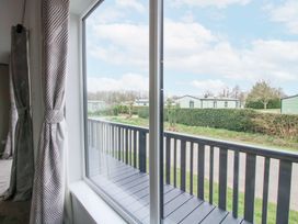 A window with patterned curtains overlooking a balcony and green mobile homes at Peony in Eardisland