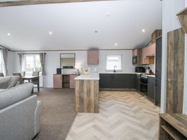 An open kitchen and living area with grey sofa dining table and wooden cabinets at Peony in Eardisland