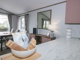 A dining area with table and chairs next to windows and a sideboard with lamp and mirror at Peony in Eardisland