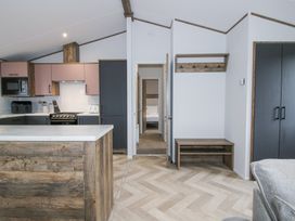 A kitchen area with wooden cabinets and a marble countertop next to a hallway leading to a bedroom and a coat rack with hooks above a bench at Peony in Eardisland