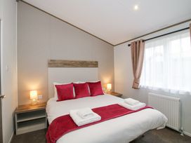 A bedroom with a double bed red cushions bedside tables lamps and window with curtains at Peony in Eardisland