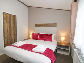 A bedroom with a bed with red pillows and runner bedside tables with lamps and a wooden door at Peony in Eardisland
