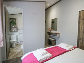 A bedroom with a bed with folded towels on a pink runner a vanity with a mirror and stool and an open door showing a bathroom with toilet and shelving at Peony in Eardisland