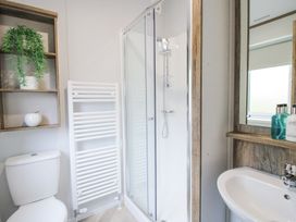 A bathroom with a toilet sink shower and a wooden wall shelf with a plant and an ornament at Peony in Eardisland