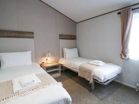 A bedroom with two single beds a nightstand with a lamp and a window with curtains at Peony in Eardisland