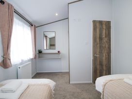 A bedroom with two beds a window with curtains a wall mirror a small shelf and a wooden door at Peony in Eardisland
