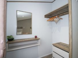 A corner of a room with a mirror above a wooden shelf and a closet with hangers and drawers at Peony in Eardisland