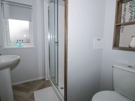 A bathroom with a shower cubicle toilet sink window and wooden wall shelves at Peony in Eardisland