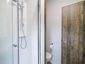 A bathroom with a shower enclosure a toilet with toilet paper and a wooden door at Peony in Eardisland