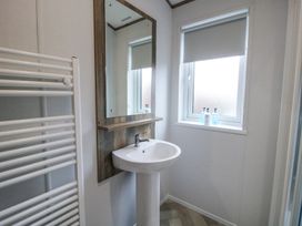 A bathroom sink with a mirror above and a window with bottles on the sill at Peony in Eardisland