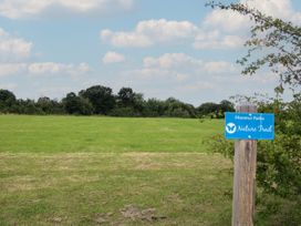 A grassy field with trees in the background and a wooden post with a blue nature trail sign at Peony in Eardisland