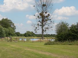 A grassy field with a fenced pond and trees under a partly cloudy sky at Peony in Eardisland