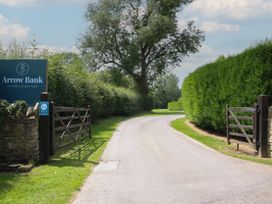 A country park entrance with wooden gates and a sign for Arrow Bank along a curved road surrounded by hedges and trees at Peony in Eardisland