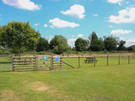 A fenced grassy area with picnic tables and trees under a blue sky at Peony in Eardisland