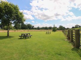 A grassy fenced field with two picnic tables and trees under a partly cloudy sky at Peony in Eardisland