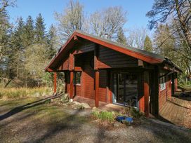 A wooden cabin surrounded by trees with a small garden and gravel area at Forsa Lodge in Glenforsa near Salen Isle Of Mull